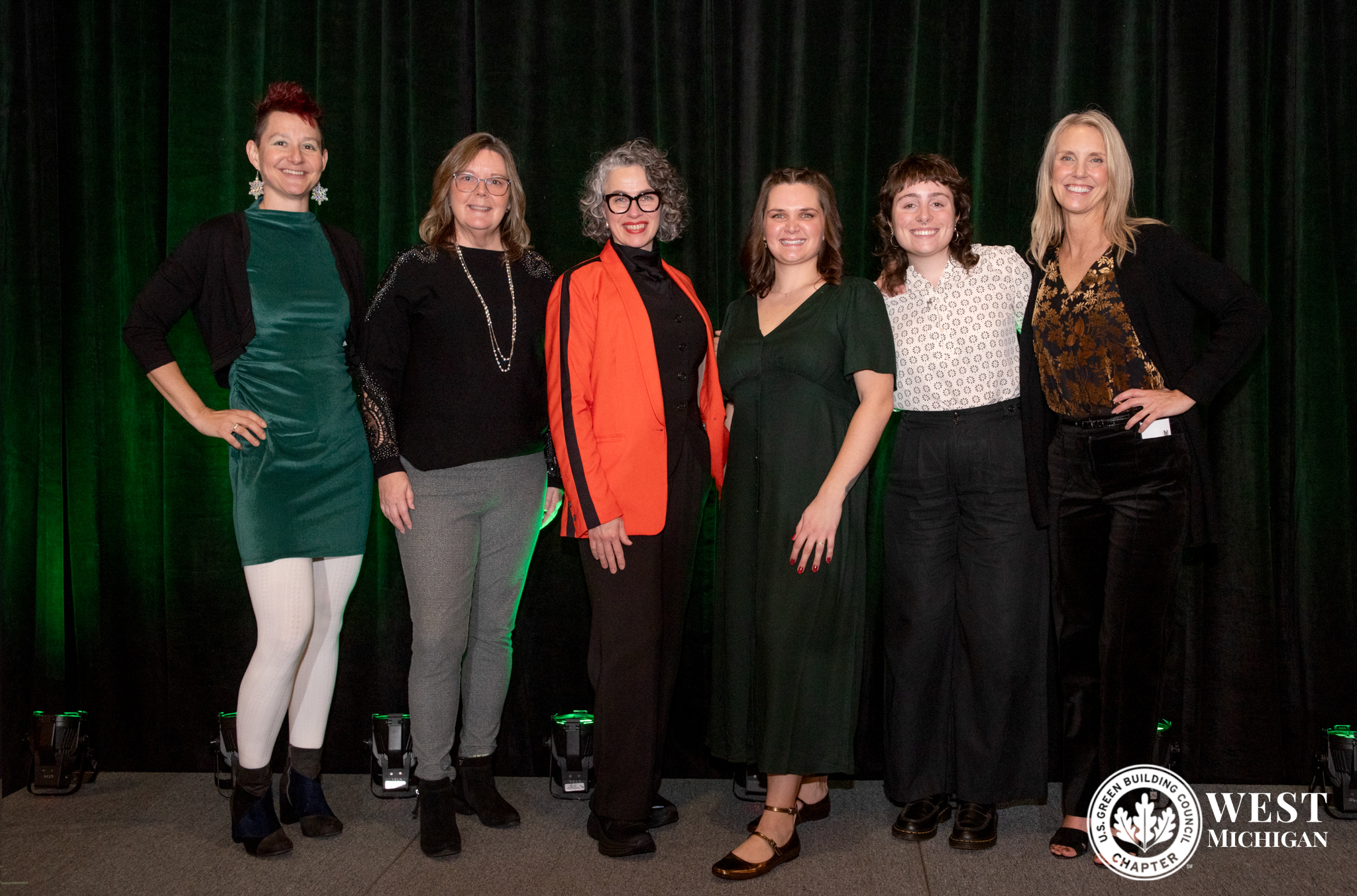 Sandra Lupien is posing with the USGBC-WM team. There are two people on the left of her and three people to the right of her. There is a dark green drape in the background.